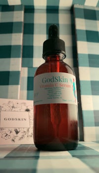 a bottle of godskin vitamin c serum sitting on top of a checkered table